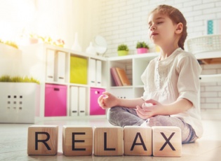 Little child girl playing with blocks and having fun. Blocks have letters. Child arranges cubes and word Relax. Girl is practicing yoga.